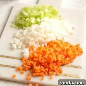 A close up of finely chopped carrot, celery and onion on a cutting board, ready for soffritto.