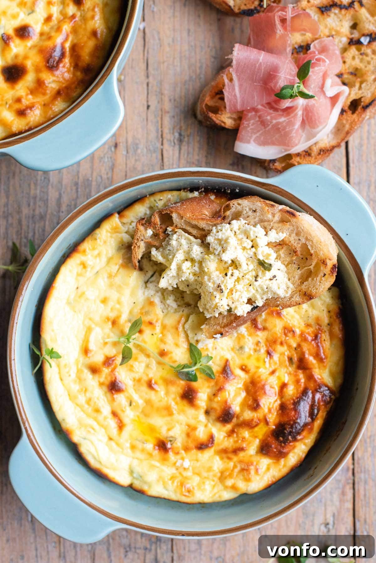 A close-up shot of baked ricotta, both in a blue baking dish and spread generously on a piece of toasted bread, garnished with fresh thyme.