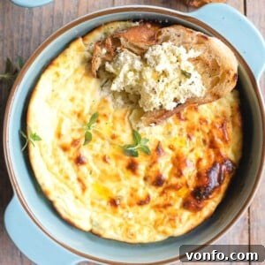 A close-up square image of baked ricotta in a blue ceramic round dish, with a piece of crusty bread dipped into it.