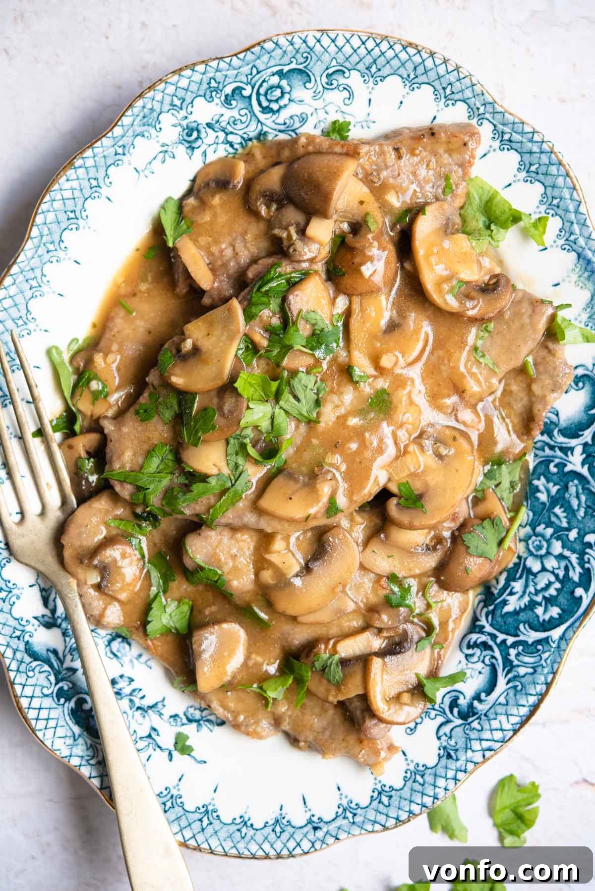 An overhead shot of classic Veal Marsala on a blue platter, garnished with sautéed mushrooms and fresh parsley, ready to be served.