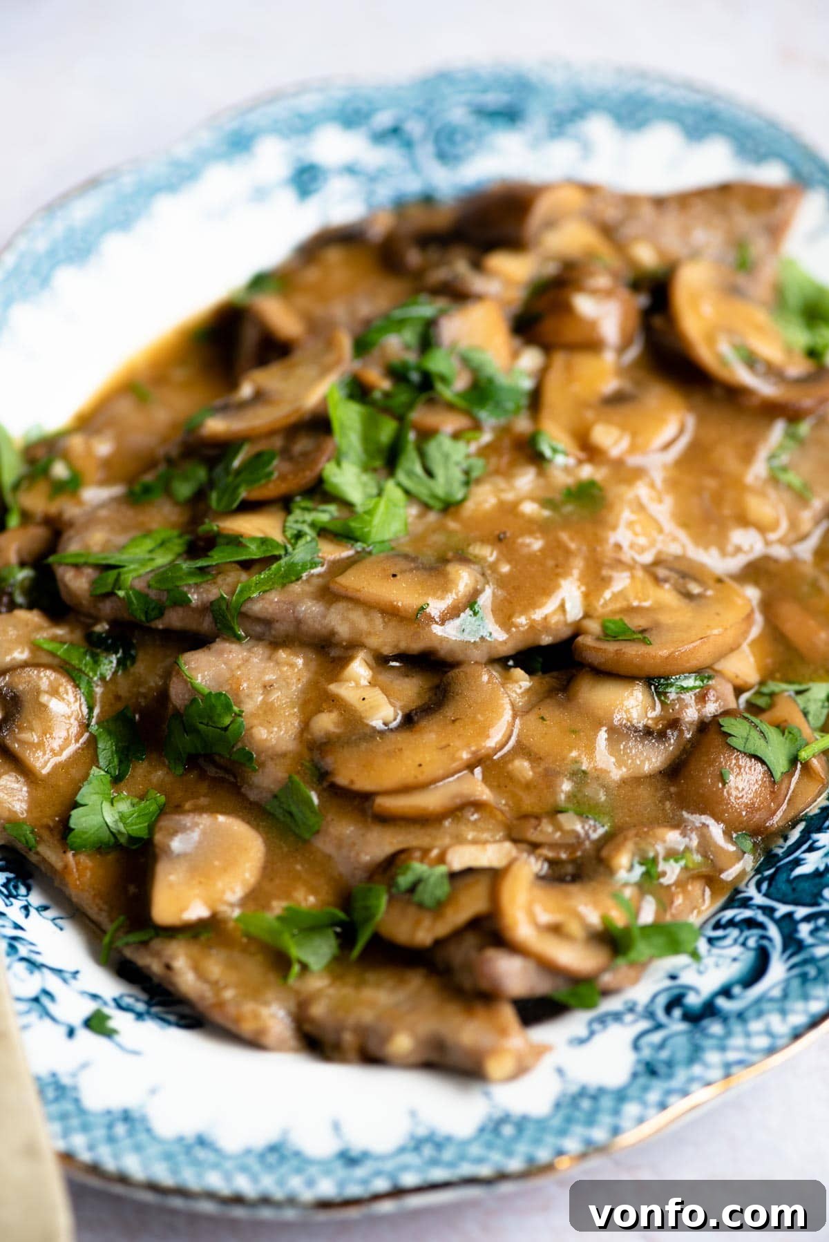 A close up of Veal Marsala with a generous amount of rich sauce, sautéed mushrooms, and fresh parsley for garnish.