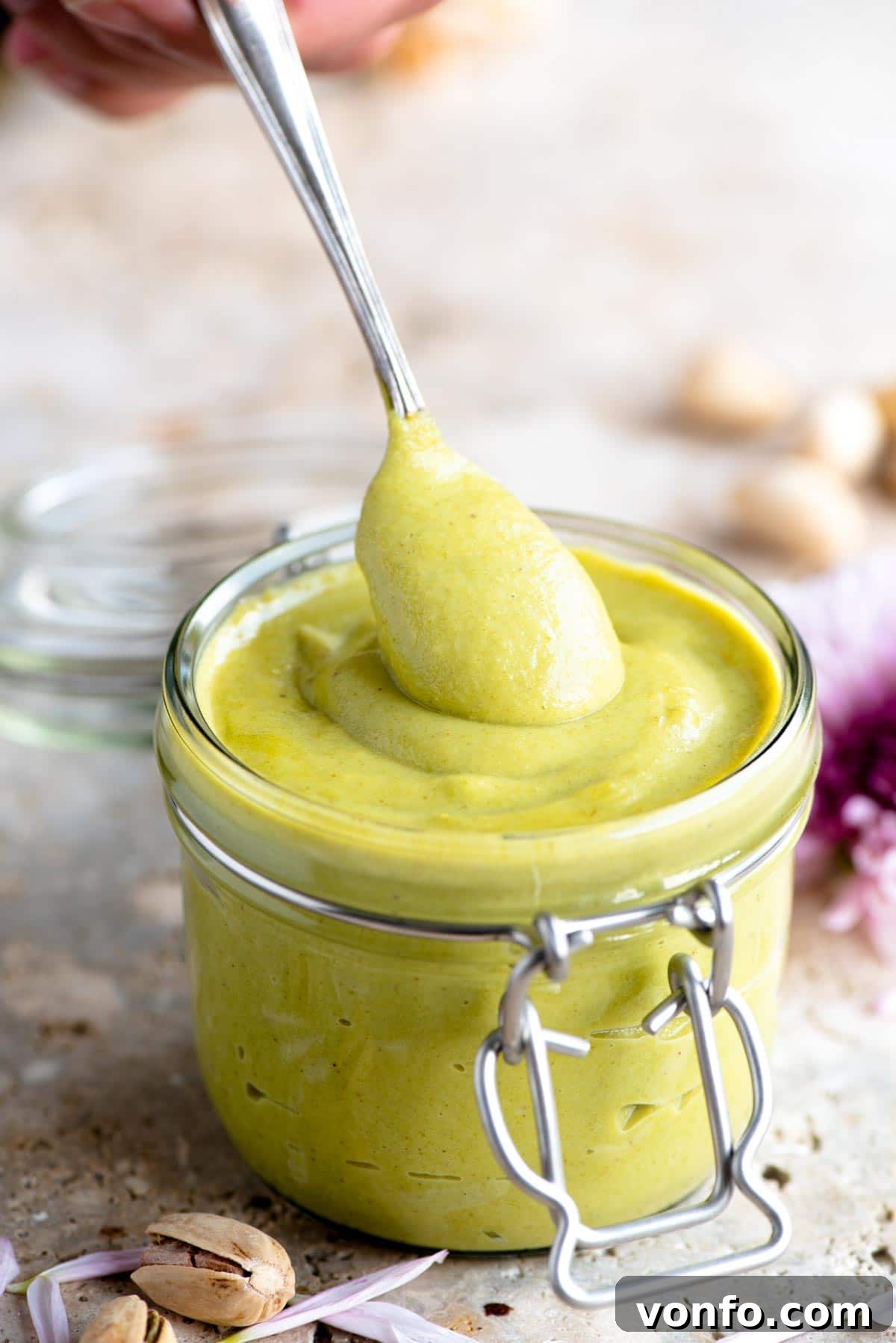 A tantalizing close-up shot of a spoonful of creamy, emerald-green Italian pistachio spread in a glass jar, inviting you to taste its rich flavor.