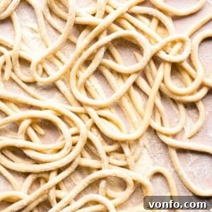 A close up of pici pasta on a neutral background