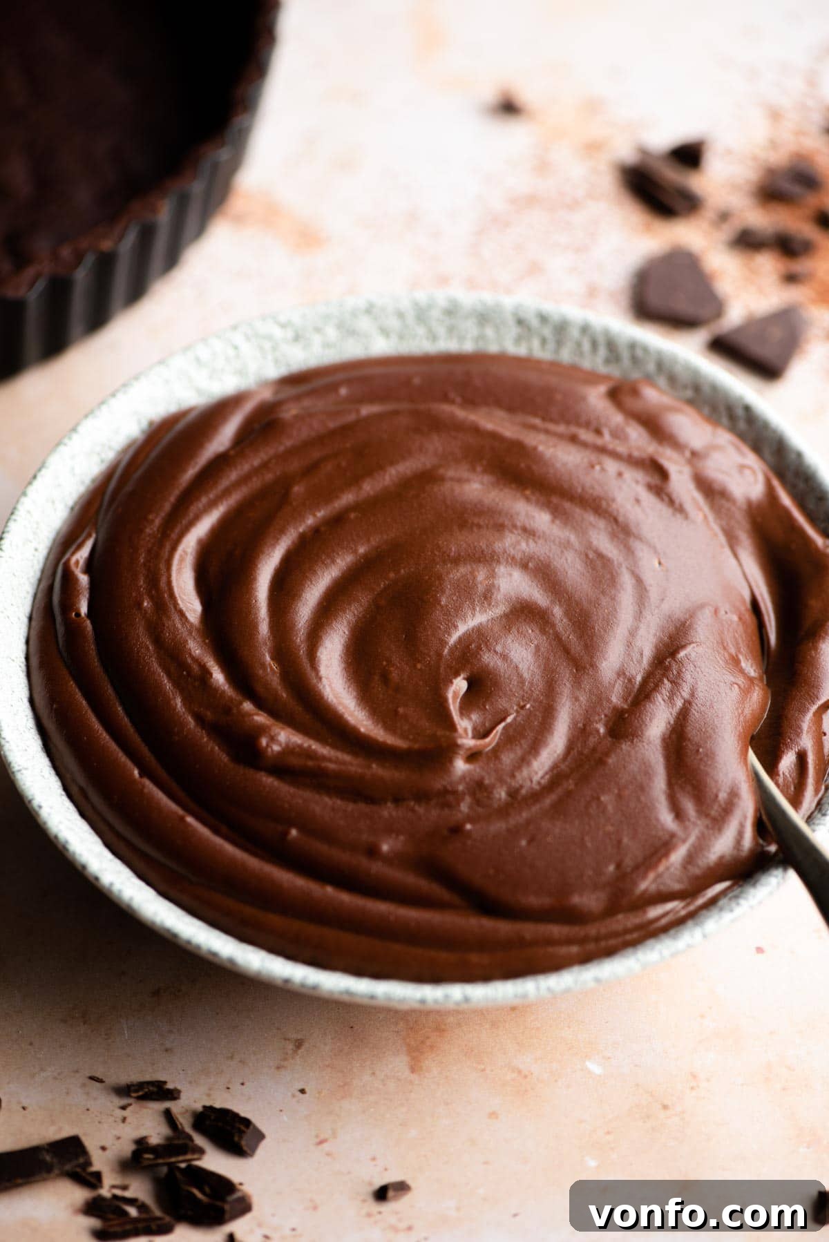 A close up of a bowl of rich, smooth chocolate pastry cream, garnished lightly with cocoa powder.