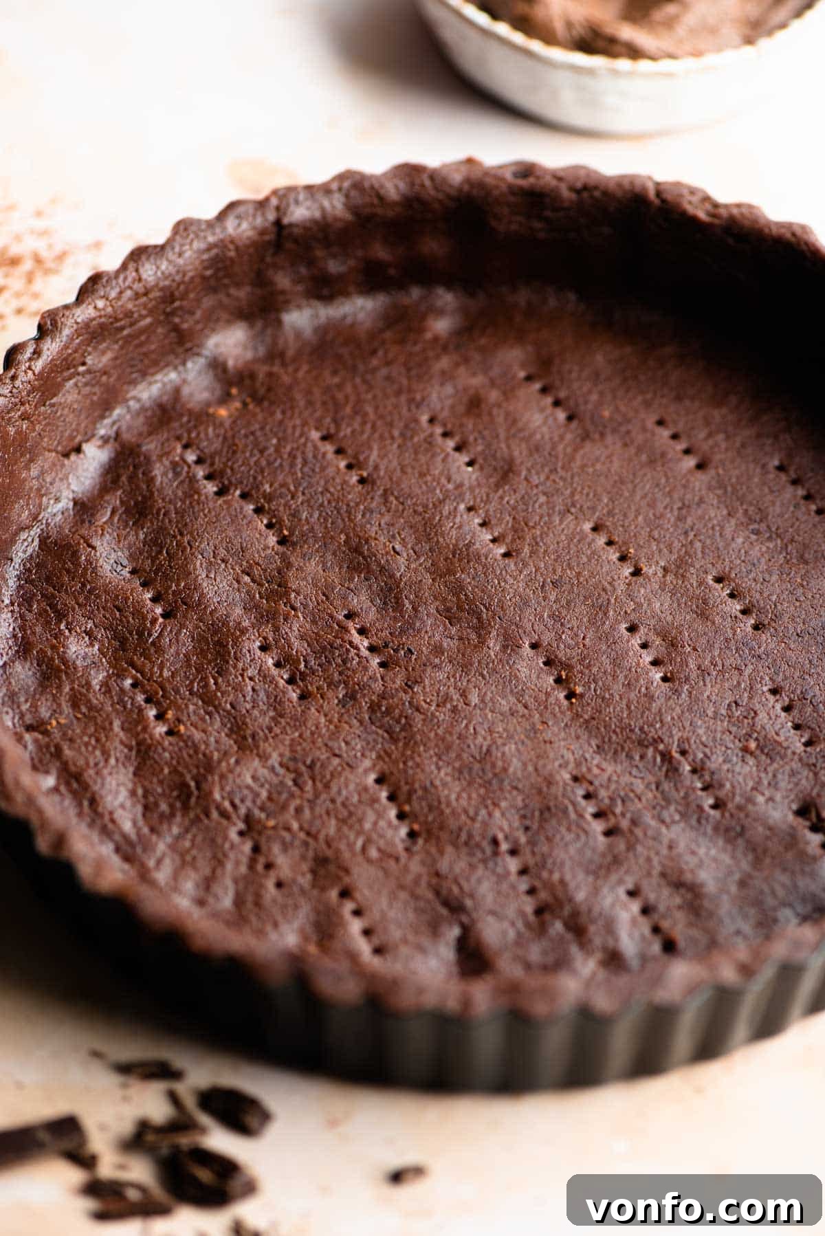 A close up of chocolate shortcrust pastry in a tart pan, emphasizing its texture and deep color