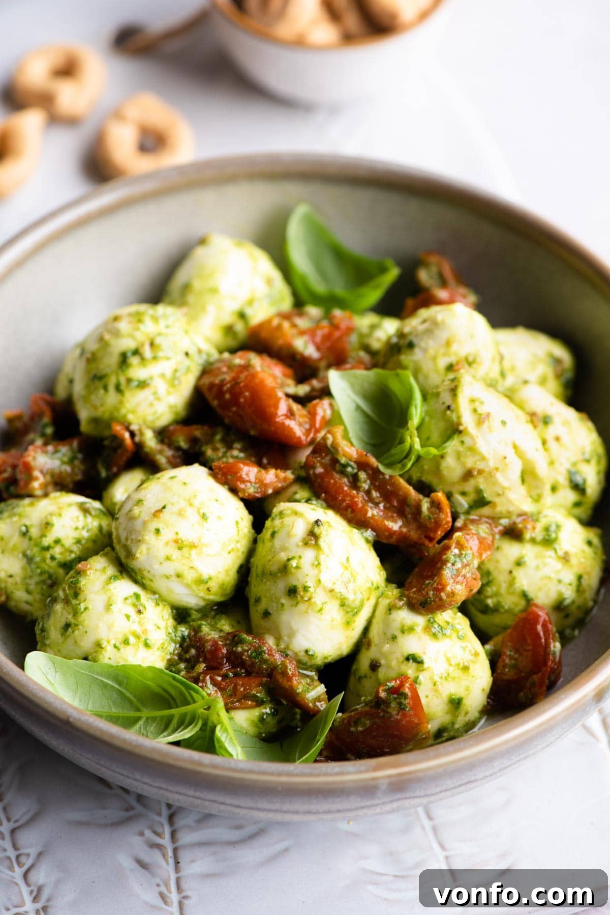 Pesto Bocconcini with Sun-Blushed Tomatoes 2 A beautifully arranged bowl of fresh mozzarella bocconcini balls, glistening with homemade green basil pesto and vibrant red sun-blushed tomatoes, ready for serving.