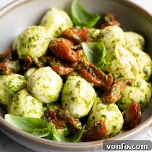 Pesto Bocconcini with Sun-Blushed Tomatoes 6 A close-up shot of mozzarella bocconcini balls lovingly coated in green pesto and nestled among sweet sun-blushed tomatoes, showcasing the vibrant colors and appealing texture.