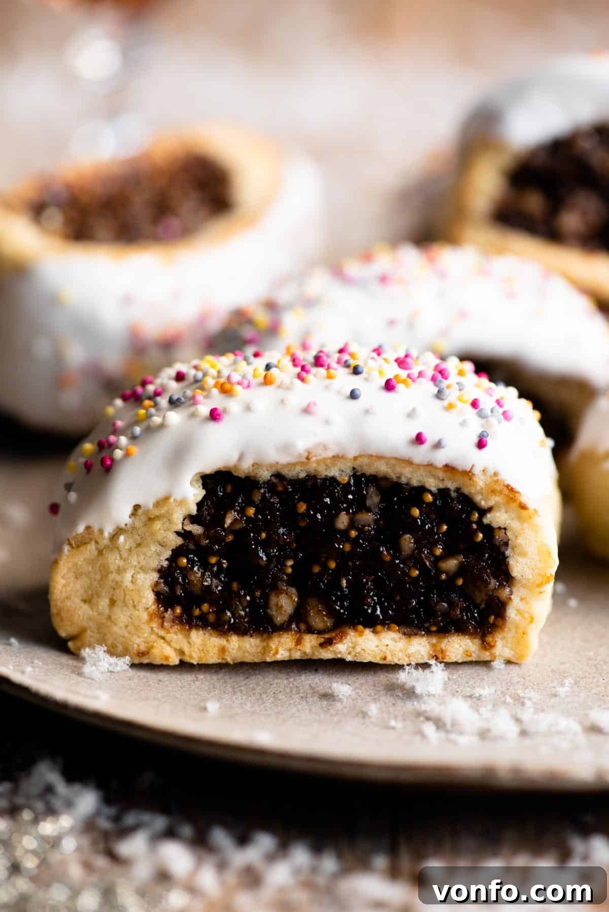 A close up of a cuccidati cookie topped with white icing and coloured sprinkles.