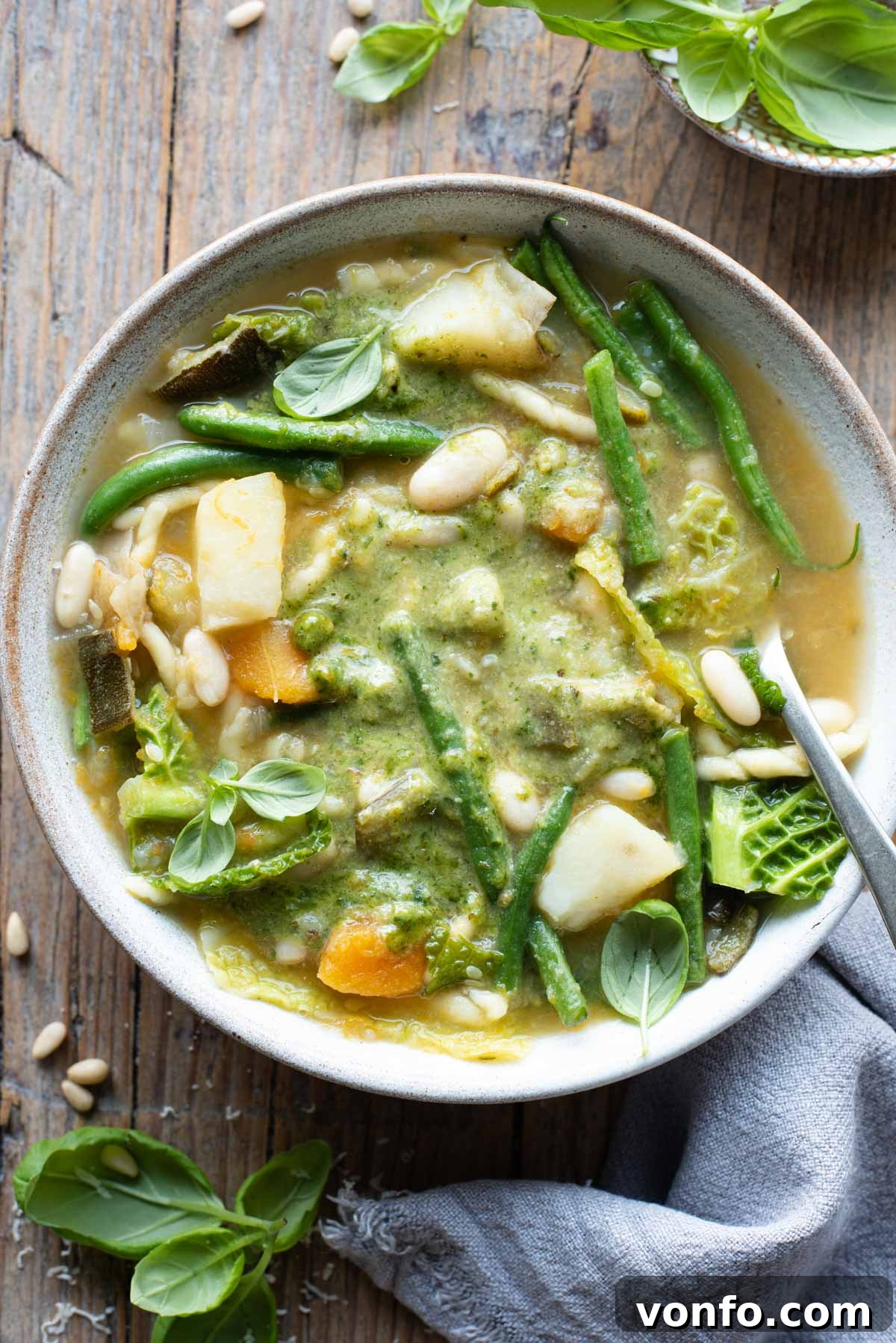 Taste of Liguria Fresh Pesto Minestrone 2 An overhead shot of a bowl of Ligurian minestrone with lots of vegetables and basil pesto sitting on a wooden background