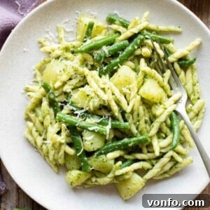 A close up of pesto pasta on a plate with potatoes and green beans
