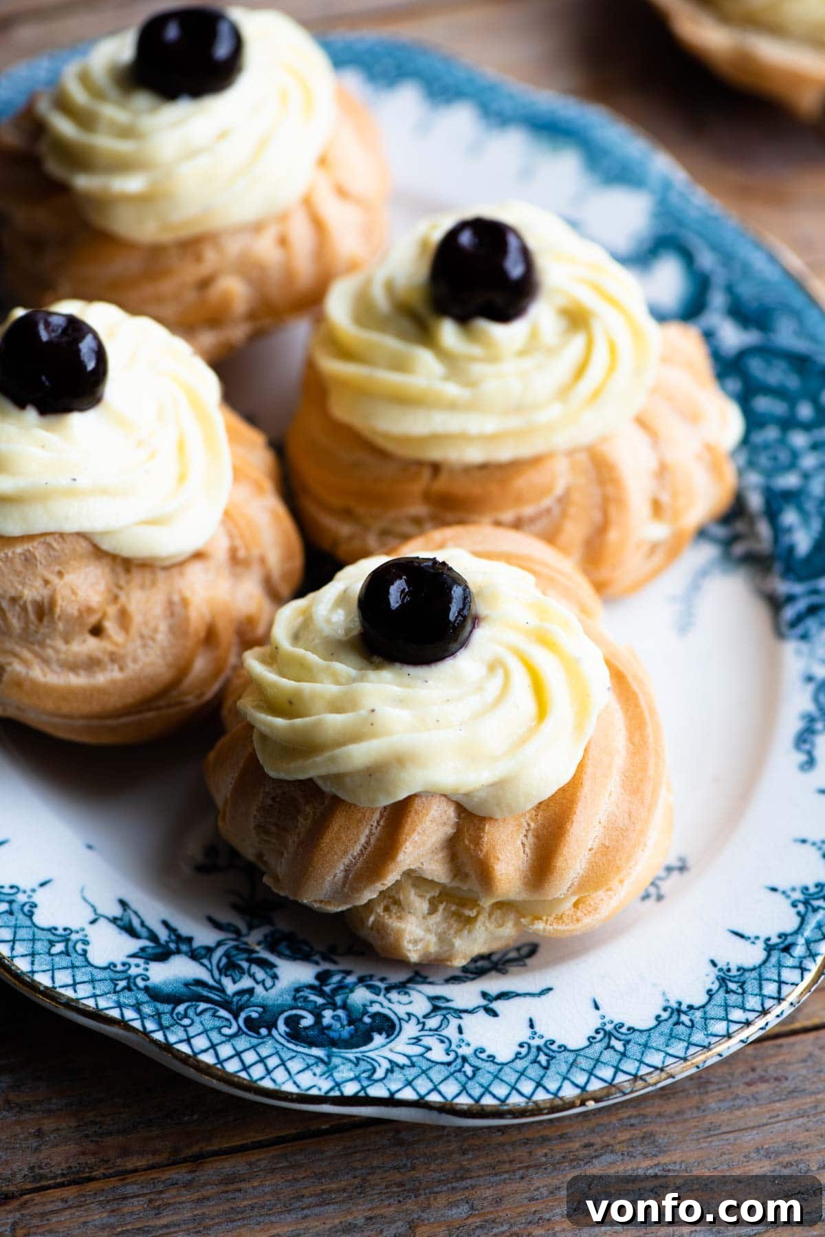 St Joseph Zeppole 2 A close up of Italian Zeppole choux buns filled with pastry cream and a cherry on top sitting on a blue and white plate.
