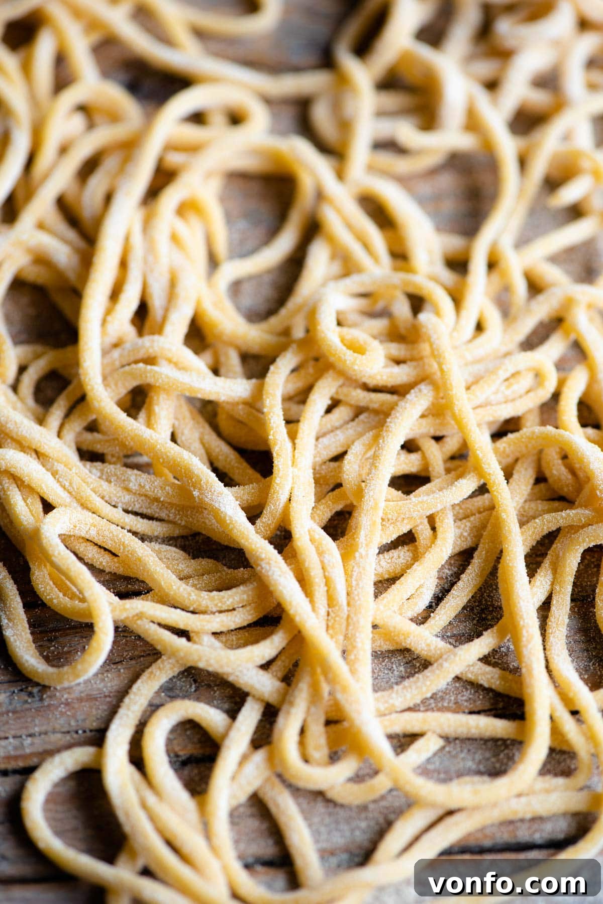 Fresh Tonnarelli: Handcrafted Chitarra Pasta 9 A close up of freshly made Tonnarelli pasta aka Spaghetti alla Chitarra scattered on a rustic wooden surface, highlighting its square edges.