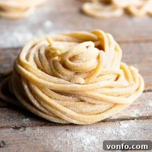 A close up of Tonnarelli pasta rolled into a nest sitting on a rustic wooden surface