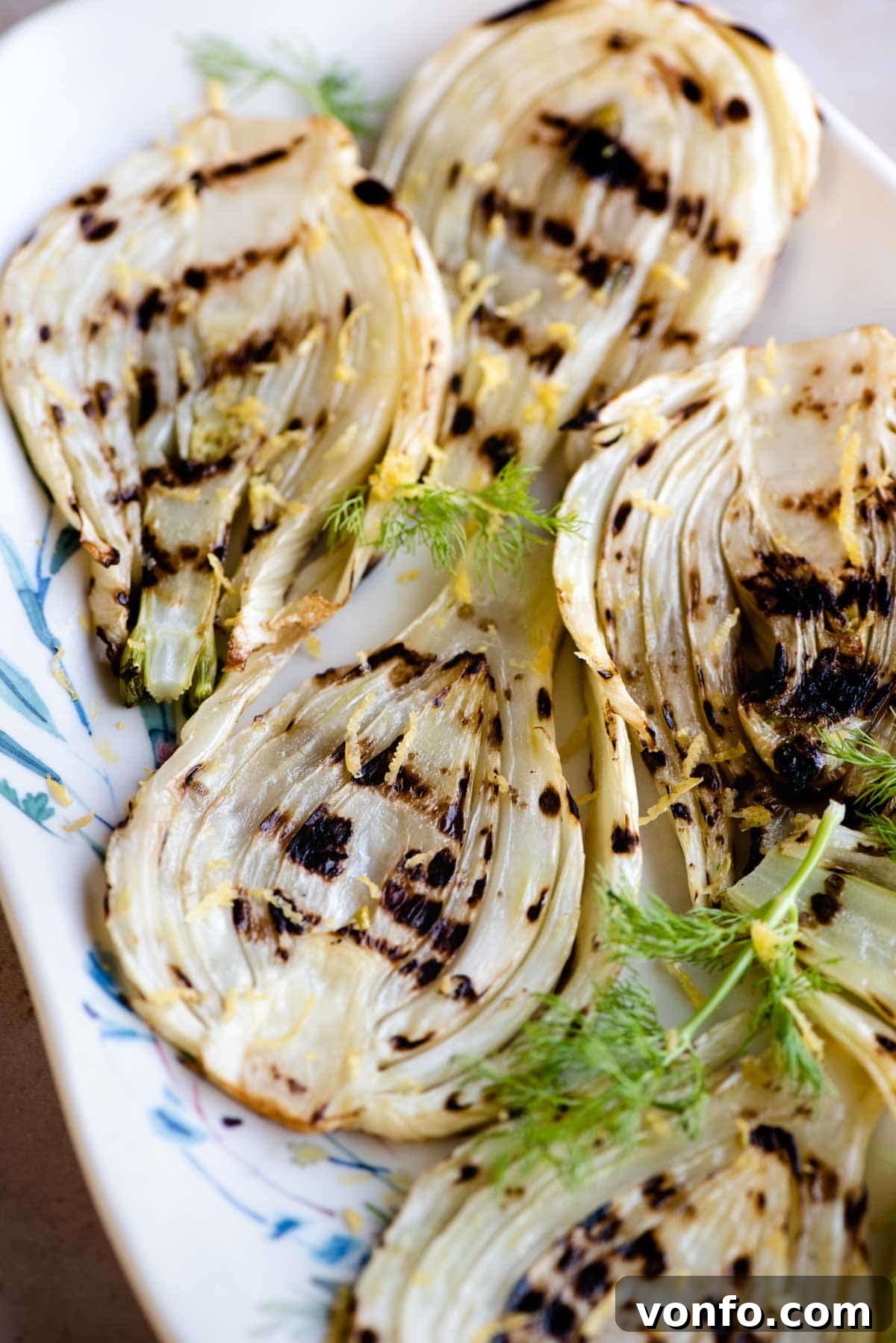 Slices of perfectly grilled fennel on a serving plate, generously garnished with fresh lemon zest and a light drizzle of olive oil.