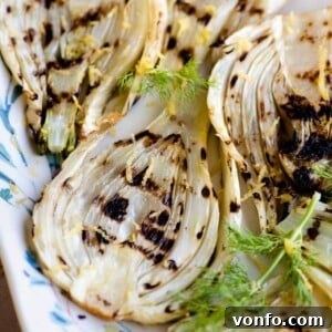 A close up of grilled fennel on a white serving plate, showing the beautiful char marks and lemon zest.