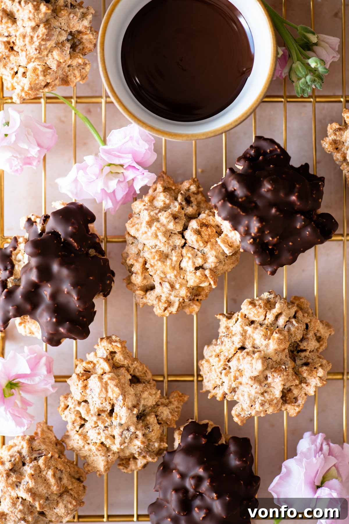 An overhead shot of both original and chocolate Brutti ma Buoni cookies on a gold cooling rack with pink flowers dotted around