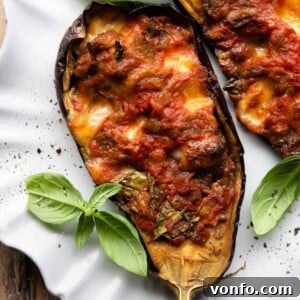Mouthwatering Italian Eggplant Boats with Mozzarella and Tomato 8 A close-up shot of a single Italian stuffed eggplant half, artfully arranged on a plate with fresh basil garnish.