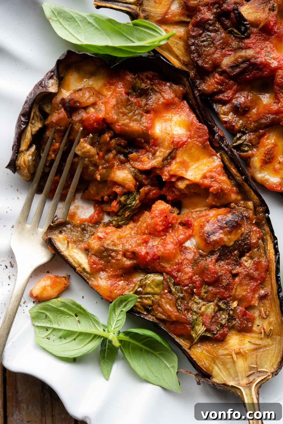 Mouthwatering Italian Eggplant Boats with Mozzarella and Tomato 7 A tantalizing close-up of a single Italian stuffed eggplant half, sliced to reveal its rich, vibrant filling of tomato, basil, and melted mozzarella, perfectly presented on a white plate.