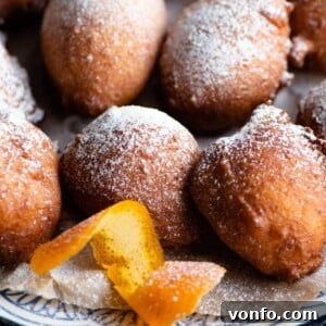 A close up of ricotta doughnuts on a plate with twisted orange peel at the side, showing their golden color and tempting appearance.