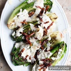 A close up of grilled romaine lettuce on a white plate topped with pancetta and Parmigiano Reggiano, showcasing its delicious texture.