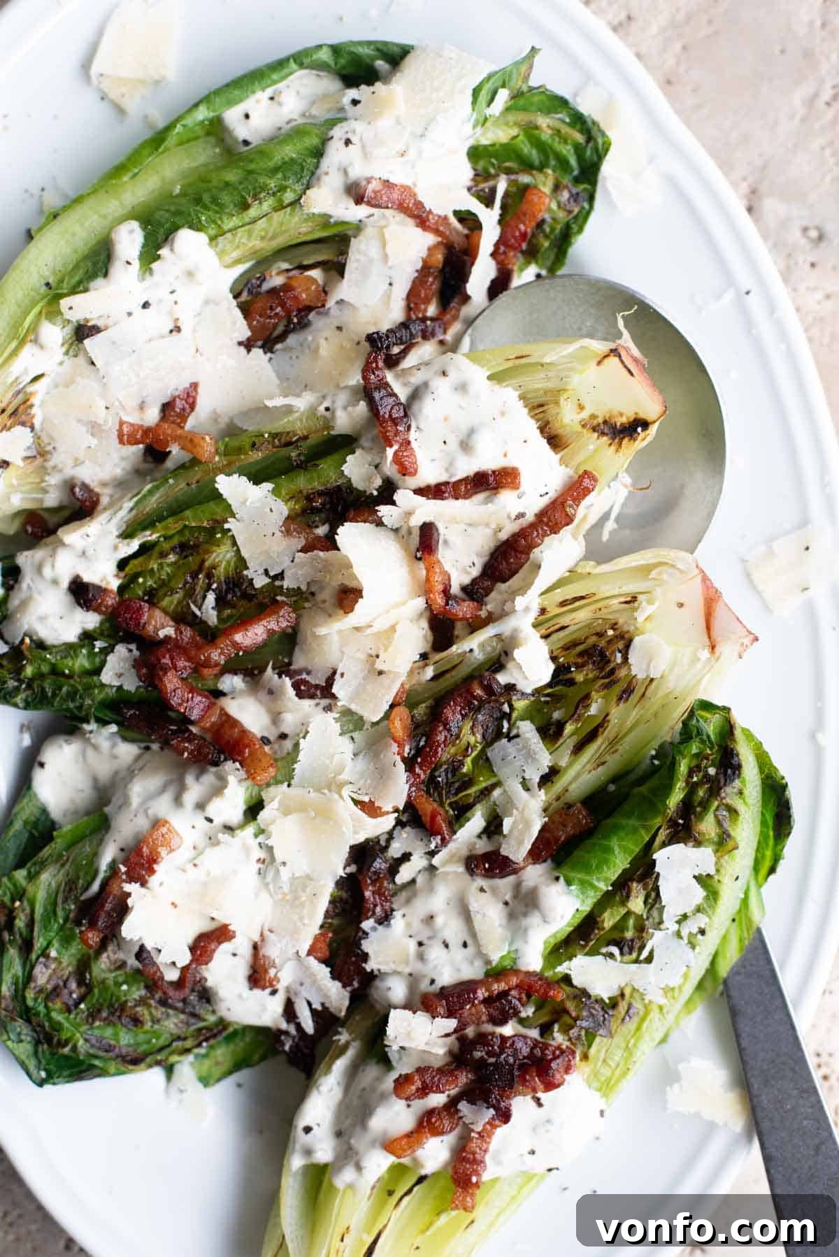 Fire-Kissed Romaine with Zesty Caper Dressing 6 A close-up overhead shot of two halves of grilled romaine lettuce, richly coated with creamy dressing and generously topped with crispy pancetta, showcasing the inviting textures and vibrant colors of the dish.