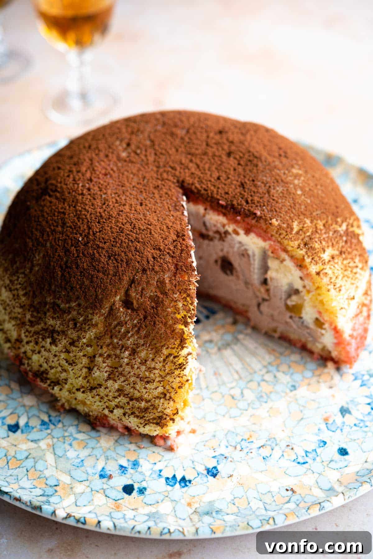 A dome shaped Italian dessert called Zuccotto on a patterned plate with a slice cut out, showcasing its layers.