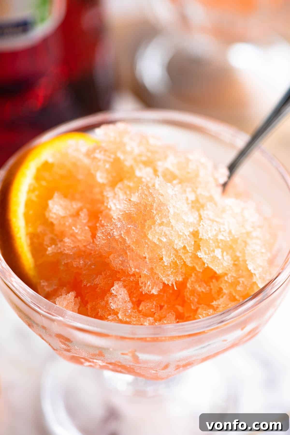 Sunset Aperol Granita 6 A close-up shot of vibrant Aperol granita served in a small glass bowl, accompanied by a spoon and a perfectly placed slice of orange on the side.