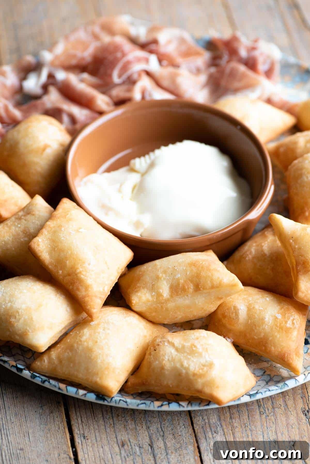 Golden Gnocco Fritto (Italian fried dough) arranged beautifully on a plate, surrounded by slices of rich cheese and delicate prosciutto.
