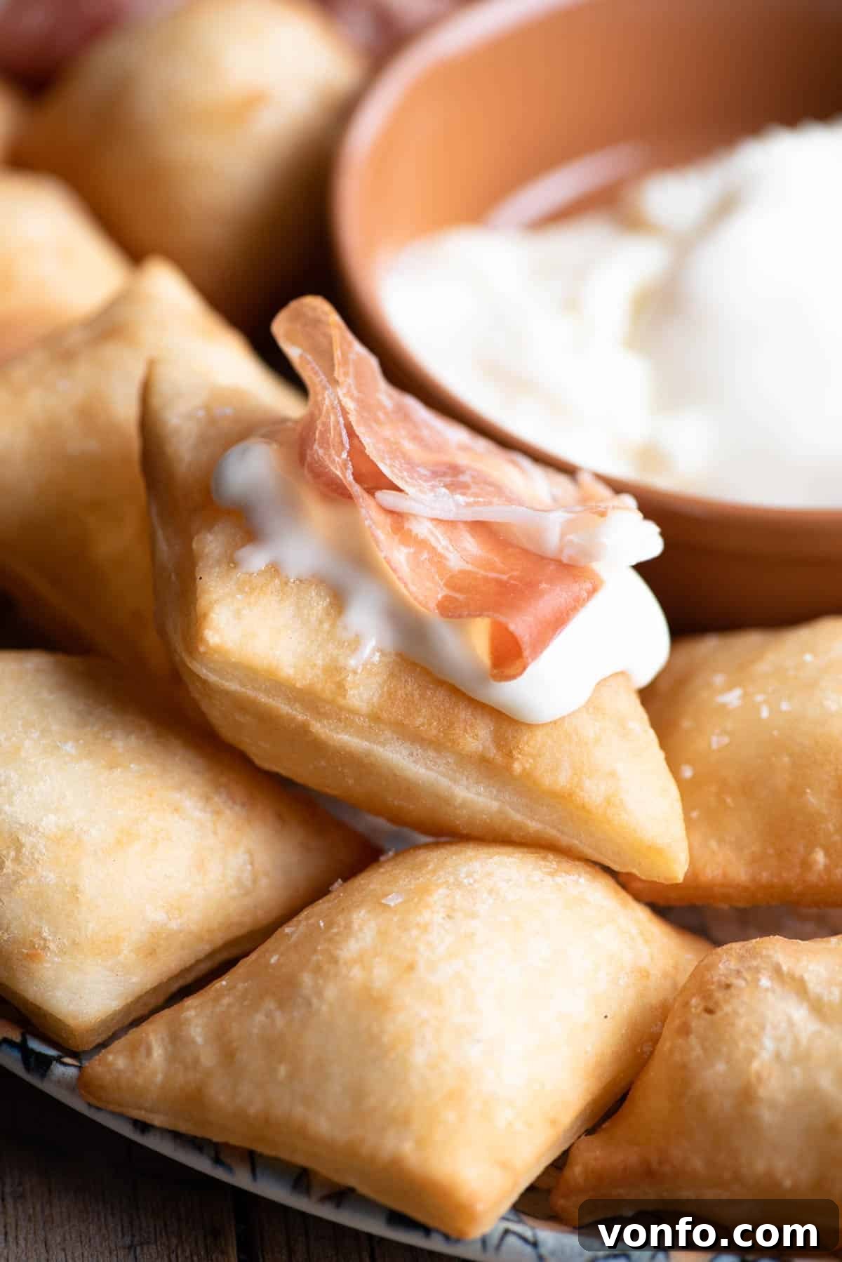 A close-up shot of crispy Gnocco Fritto (Italian fried dough) adorned with rich cheese and thin slices of prosciutto, ready to be enjoyed.