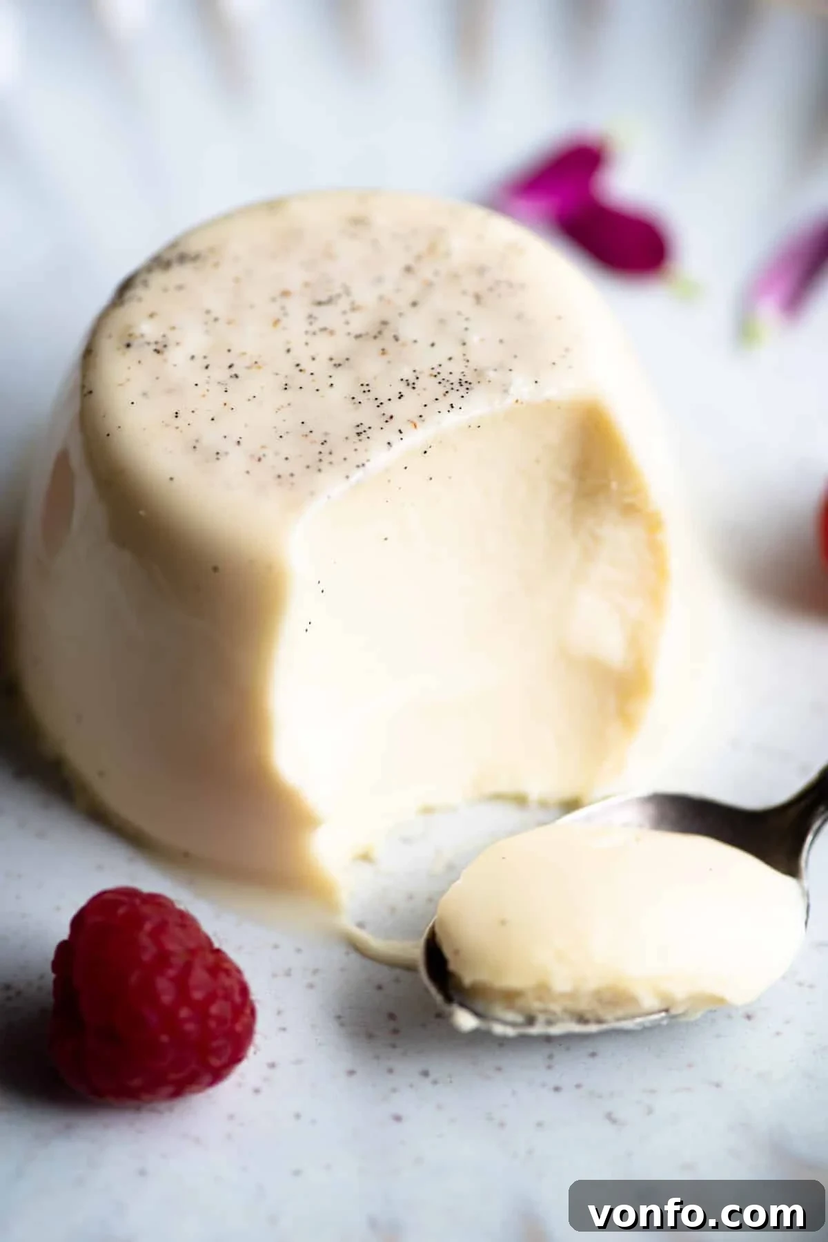A close up of a vanilla panna cotta with a bite out and spoon at the side.