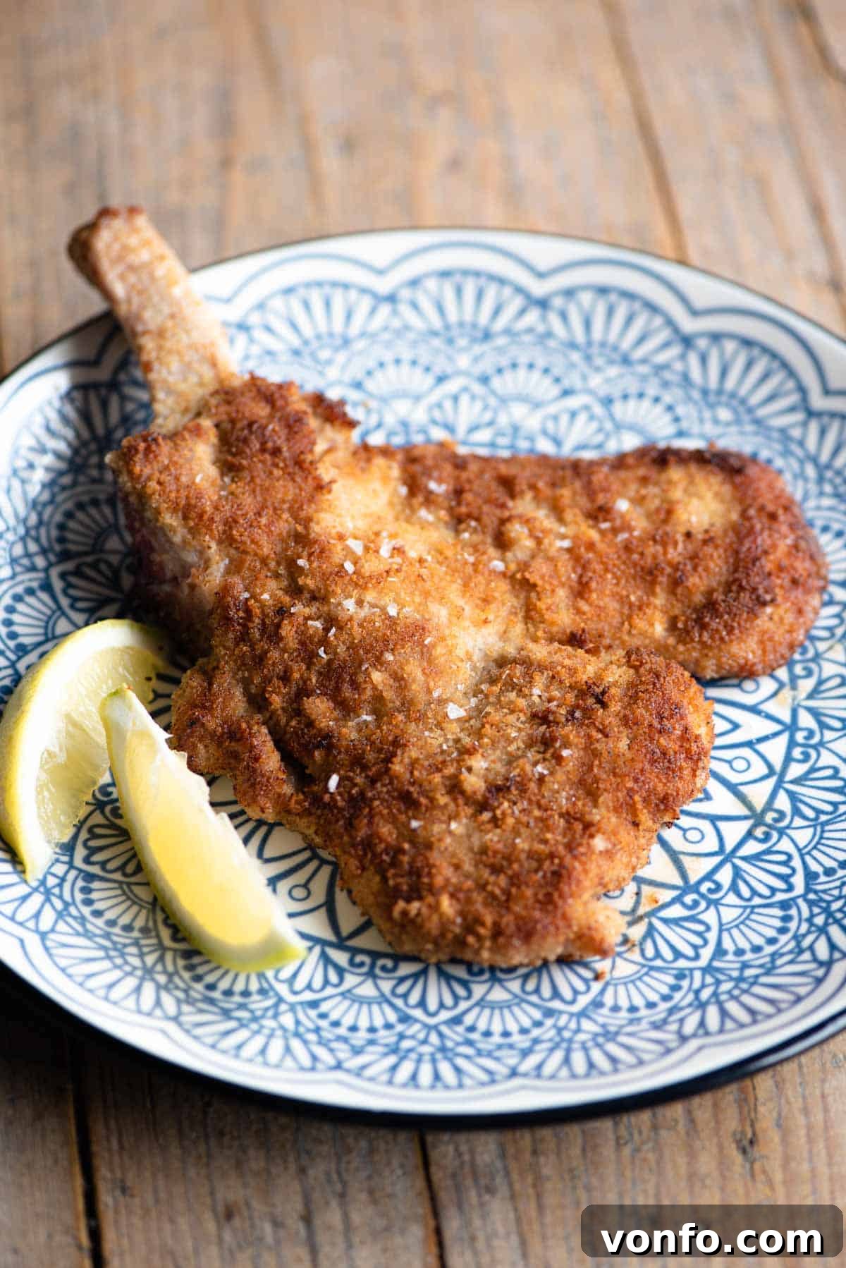 Veal Milanese 2 Crispy Veal Milanese (veal cutlet) on a blue plate with fresh lemon wedges, ready to be served.