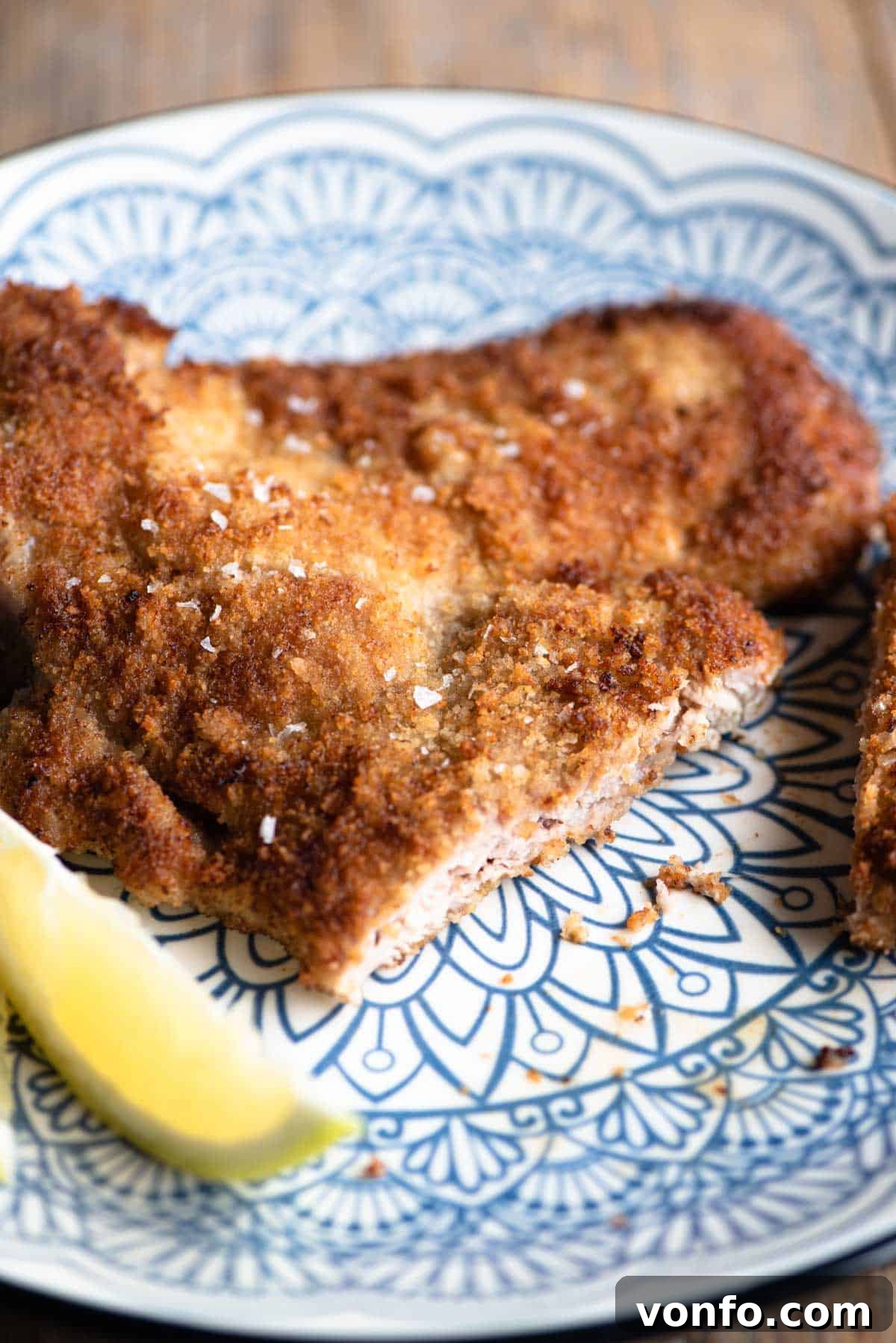Veal Milanese 6 A close-up shot of a perfectly cooked Veal Milanese on a plate, showing the crispy texture and a slice cut open to reveal the tender veal inside.