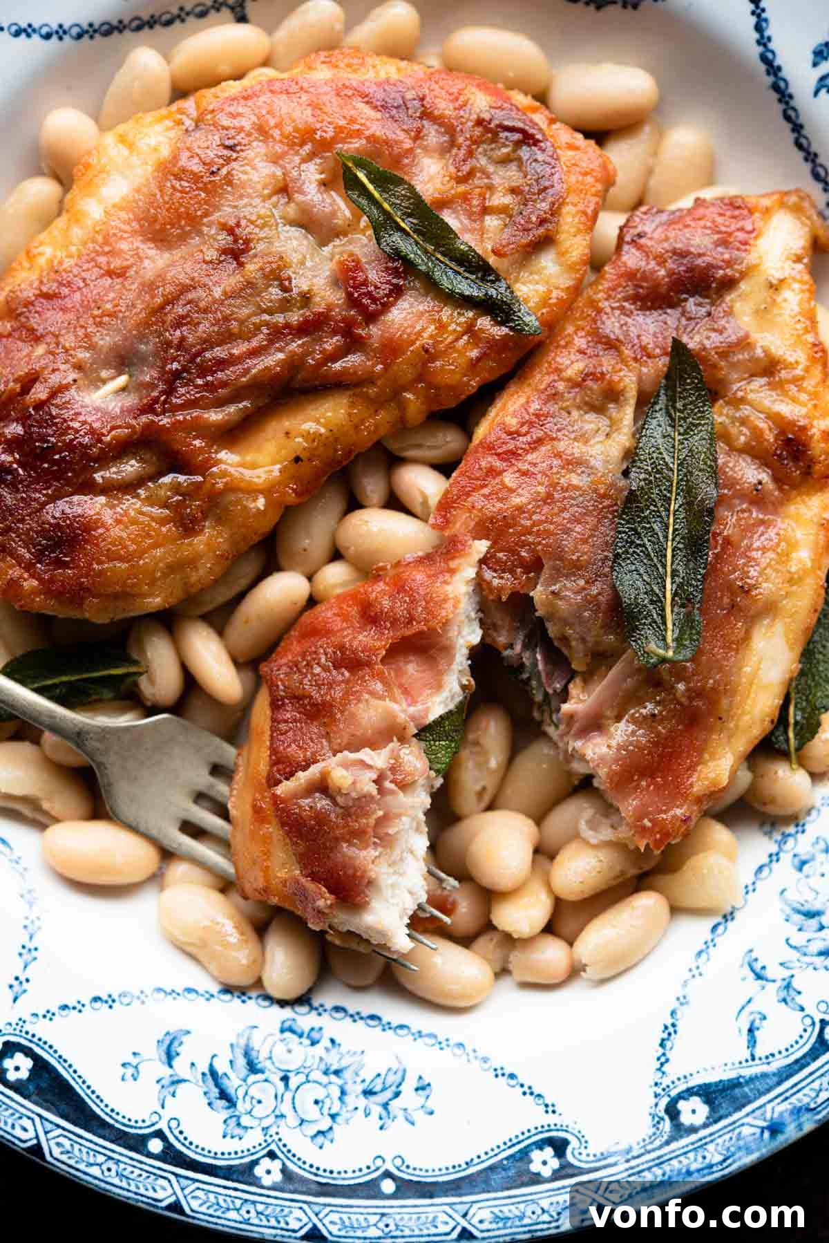 A close-up shot of crispy Chicken Saltimbocca, garnished with fresh sage, on a plate with rosemary cannellini beans, highlighting the texture and presentation.