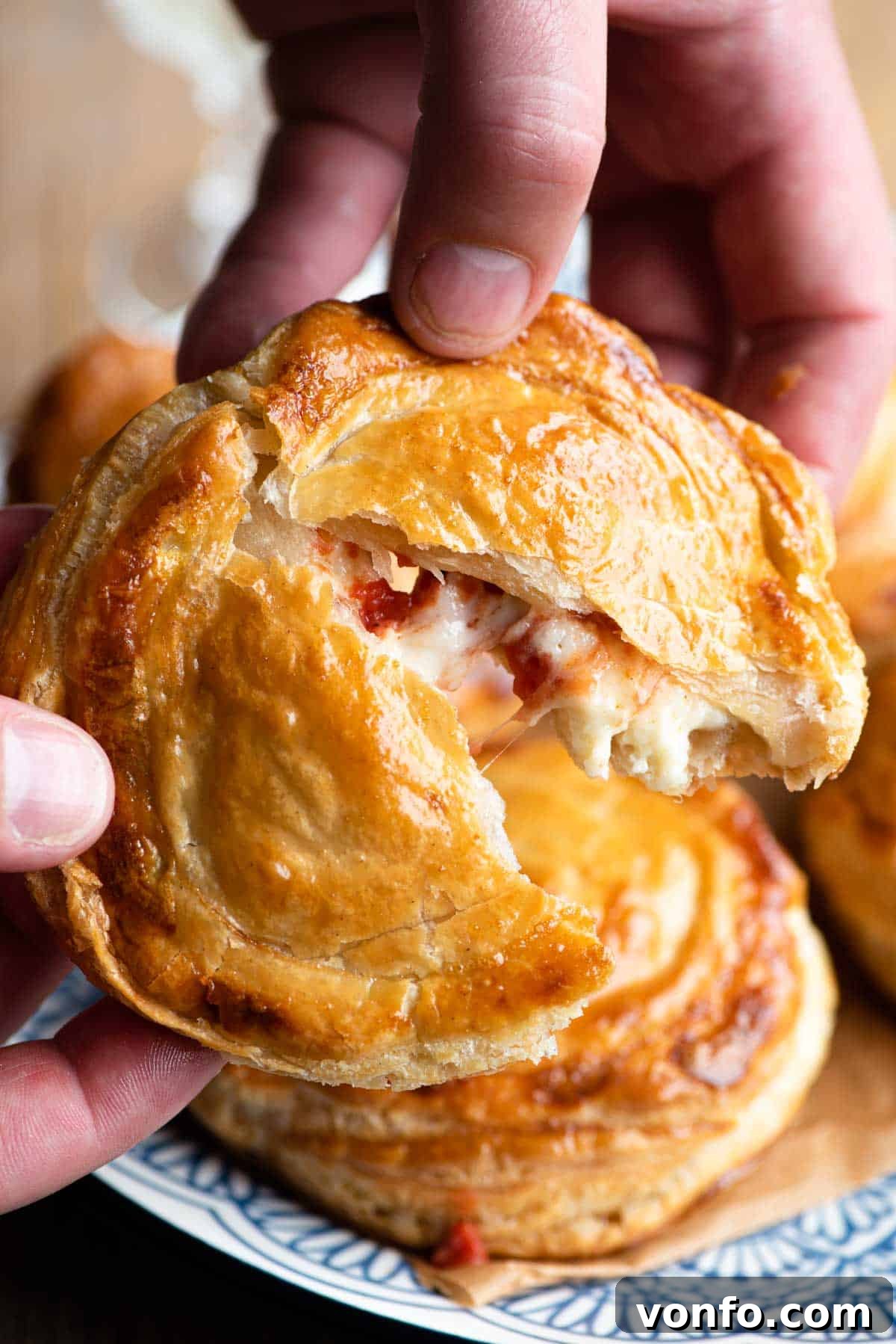 Two hands gently tearing open a Rustico Leccese, revealing a warm, cheesy tomato filling oozing out from the flaky, golden pastry.