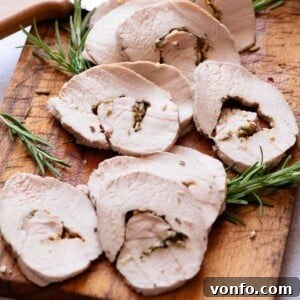 A close up cropped image of roast pork loin sliced on a wooden board, ready to serve.