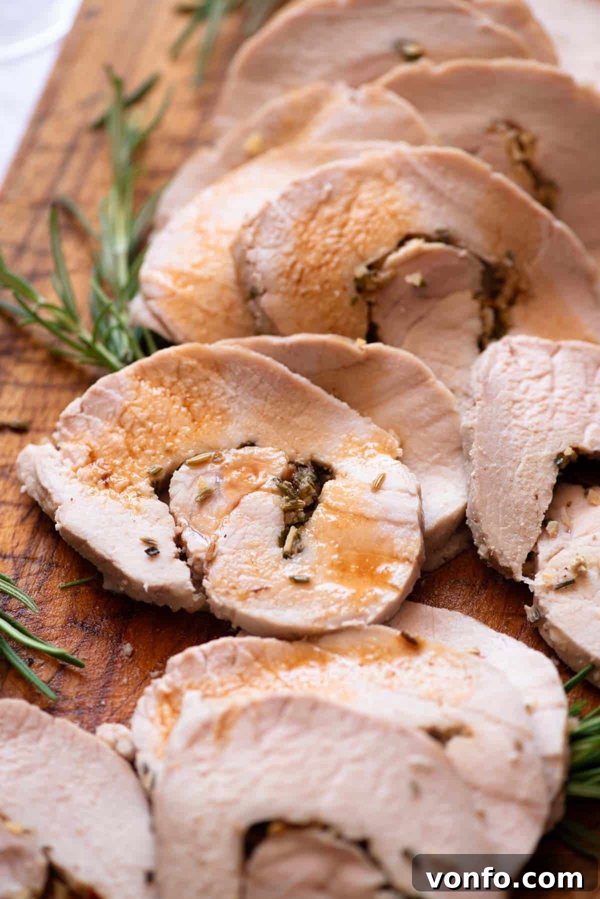 A close-up of a beautifully roasted Italian stuffed pork loin, sliced and drizzled with its savory pan juices on a wooden board.