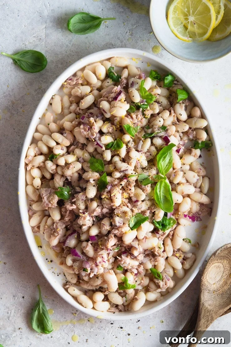 An overhead shot of a vibrant white bean salad with tuna and basil served on an elegant oval plate, highlighting its fresh ingredients and inviting texture.
