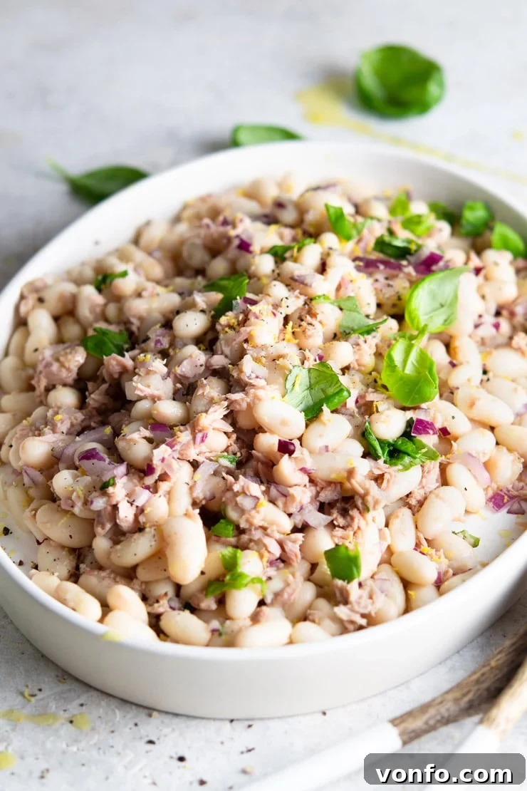 A side shot of a creamy white bean salad with tuna and fresh basil, beautifully presented on a pristine white serving plate.