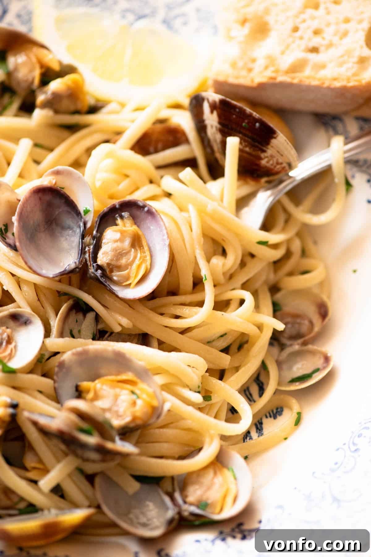 A close up of linguine pasta with clams, parsley and lemon in a bowl.