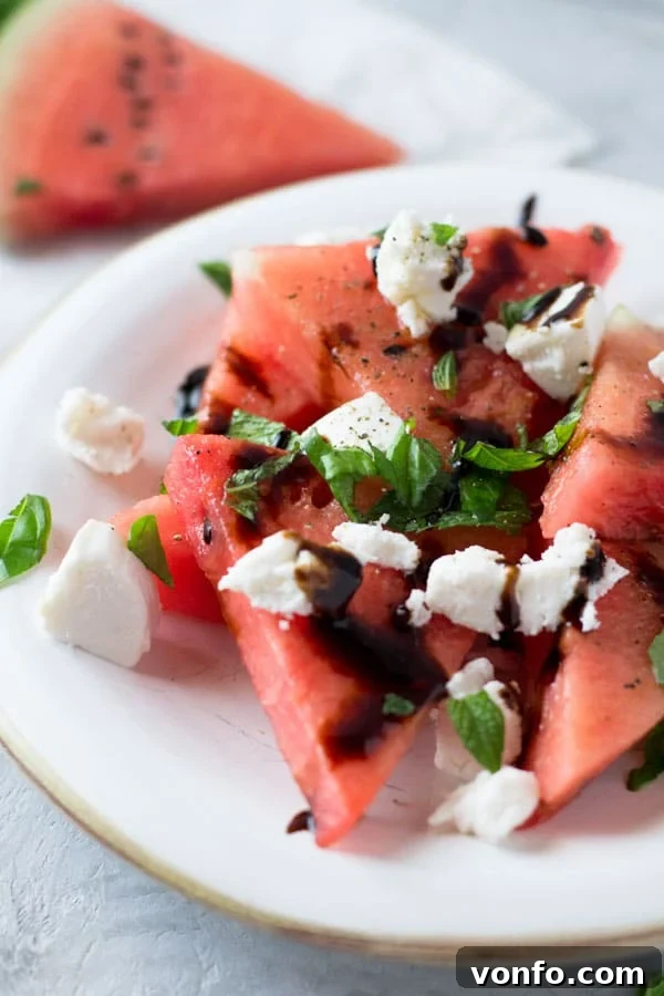 Close-up of a refreshing watermelon, basil, mint, and goat cheese salad, showcasing the vibrant colors and balsamic drizzle. Healthy summer food inspiration.