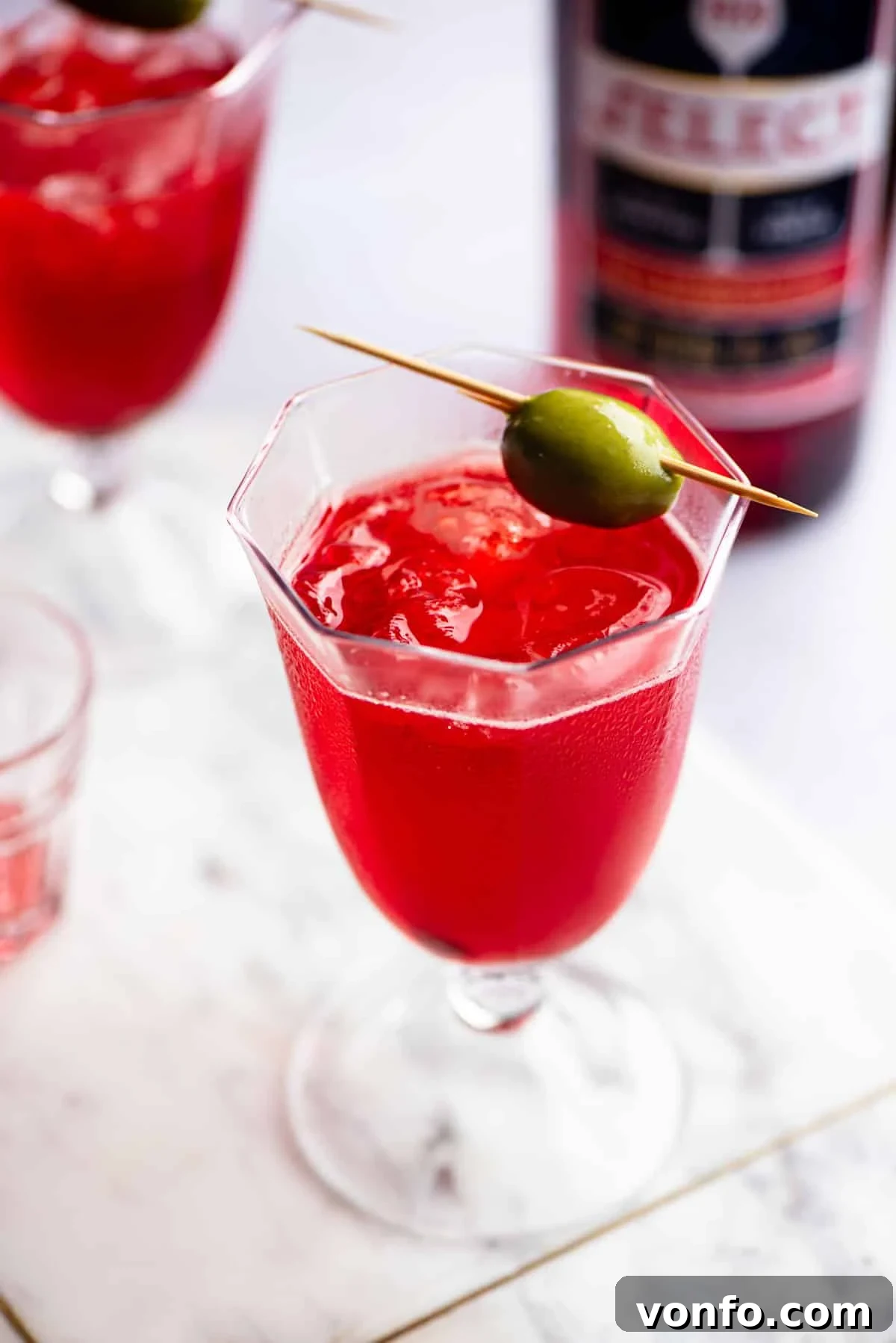 A close up of a Venetian Select Spritz on a marble chopping board topped with an olive, highlighting the rich color.
