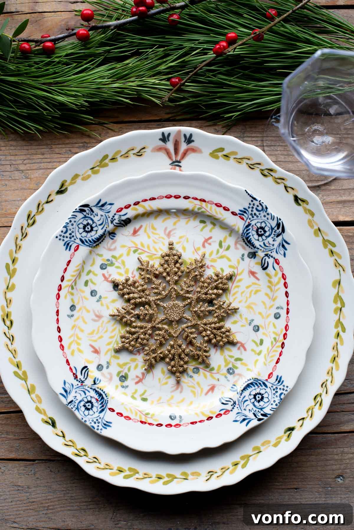 A beautifully set Christmas table with elegant Christmas plates, festive glassware, and natural foliage adorning a rustic wooden surface, inviting guests to a holiday feast.