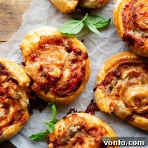 A close up overhead shot of pizza pinwheels on a sheet of baking parchment with basil leaves.