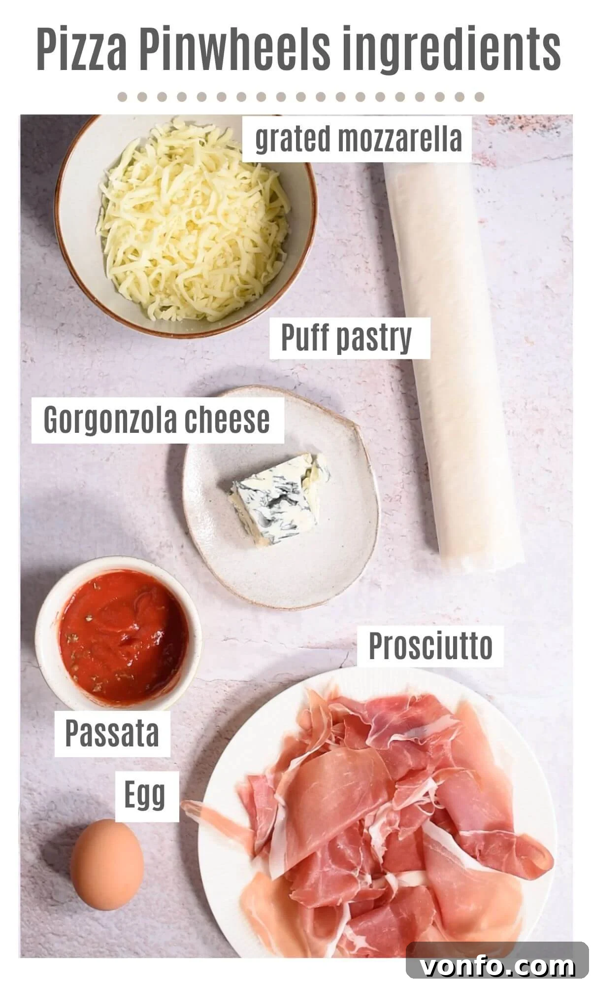 Prosciutto Gorgonzola Pizza Swirls 3 A selection of fresh ingredients laid out on a clean surface, including a sheet of puff pastry, passata, dried oregano, slices of prosciutto, crumbled Gorgonzola, and shredded mozzarella, ready for making pizza pinwheels.