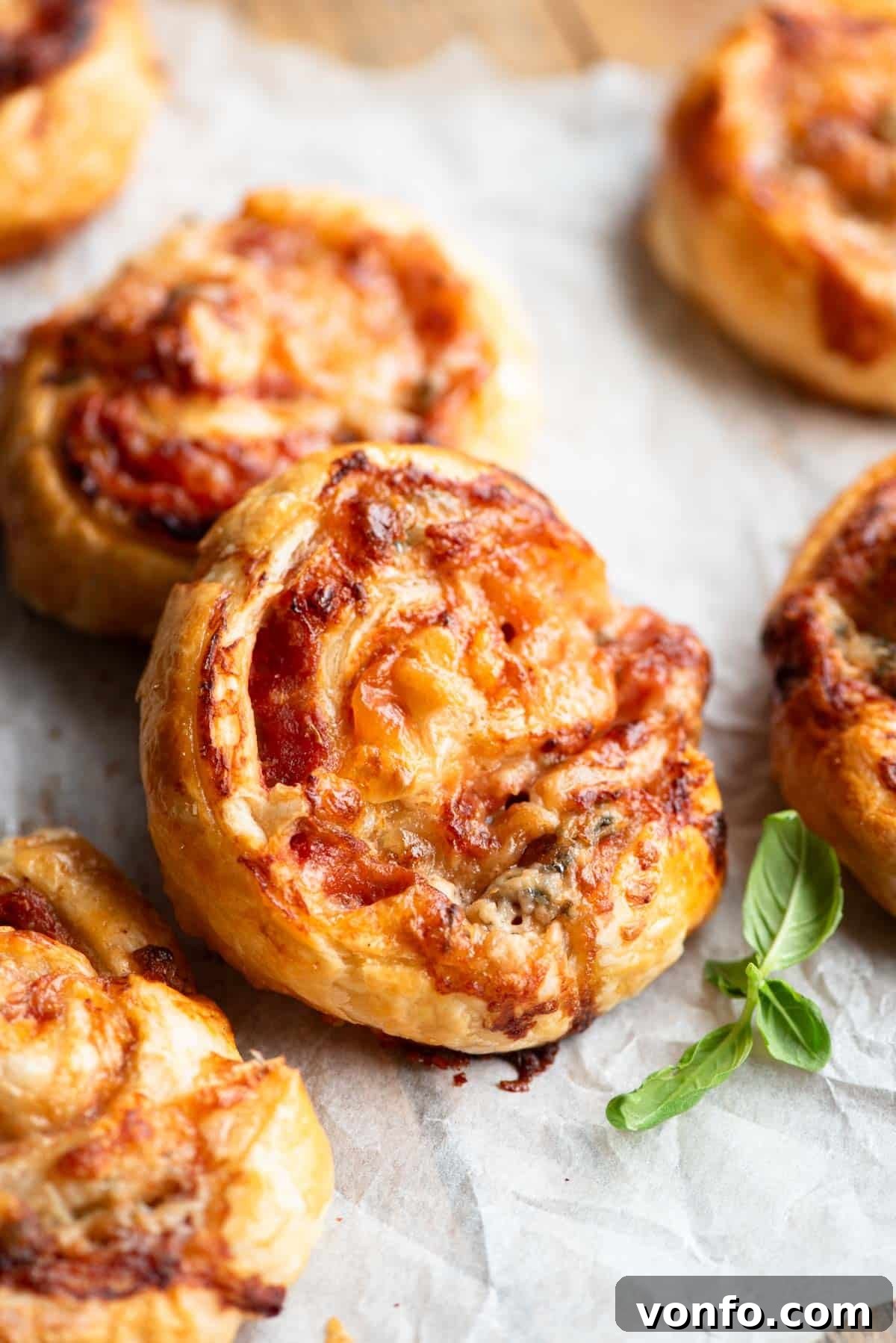 Prosciutto Gorgonzola Pizza Swirls 6 A close-up shot of freshly baked pizza pinwheels, showcasing their golden, flaky crust and melted cheese, resting on a wooden board.