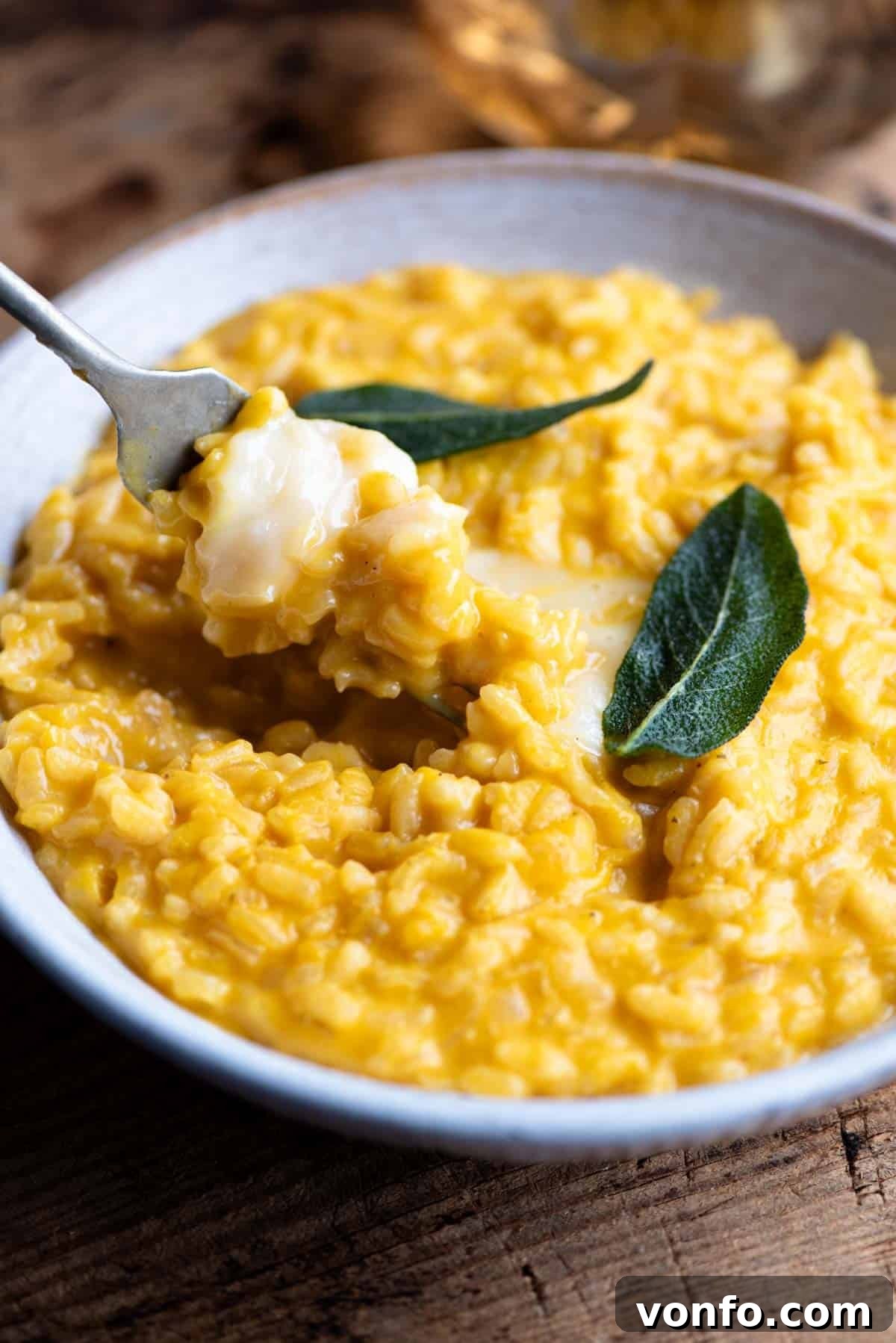 Creamy Taleggio Pumpkin Risotto, Crispy Sage Finish 8 A close-up side shot of a spoonful of creamy Pumpkin Risotto, showcasing the melted Taleggio cheese oozing from the rich orange rice and garnished with a crispy sage leaf.