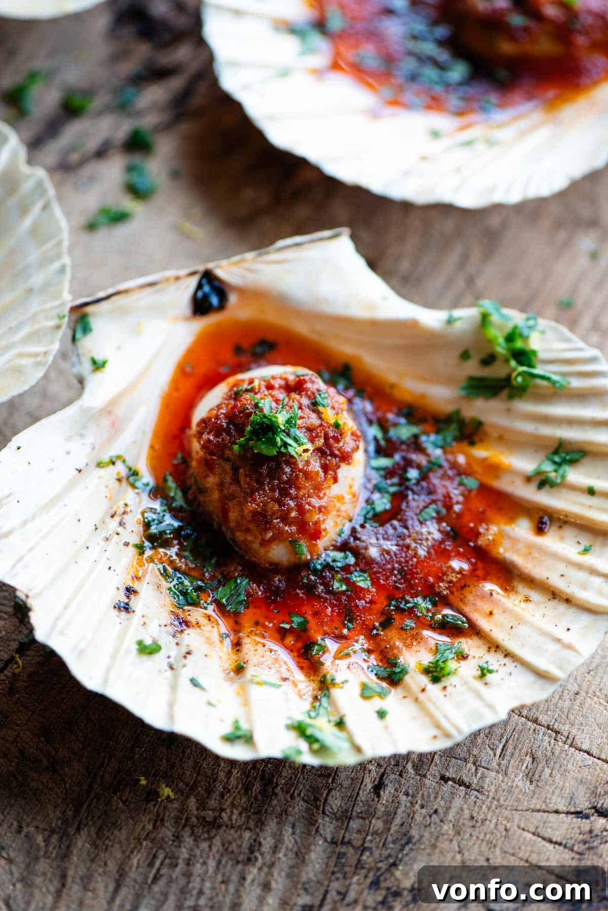 'Nduja Garlic Butter Scallops 6 A close-up, mouthwatering side shot of a single scallop beautifully presented in its shell, adorned with melted 'Nduja garlic butter and a fresh parsley garnish.