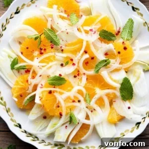 A close-up overhead shot of a vibrant Sicilian Fennel and Orange Salad on a plate, garnished with pink peppercorns and fresh mint.