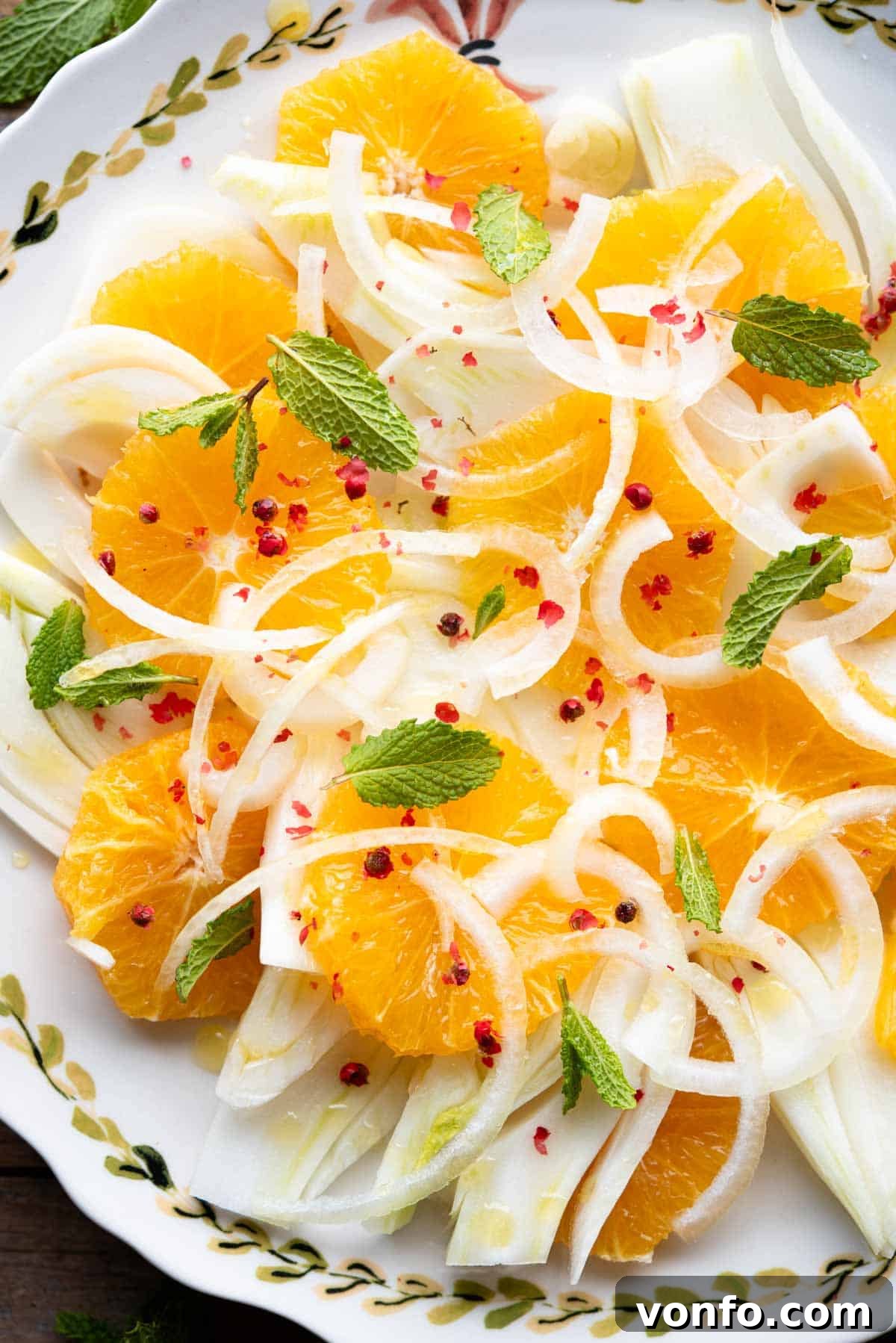 Zesty Sicilian Fennel Orange Salad 6 A close-up of a vibrant Sicilian Fennel and Orange Salad, featuring crisp fennel, juicy orange slices, thinly sliced white onion, fresh mint leaves, and a sprinkle of pink peppercorns.