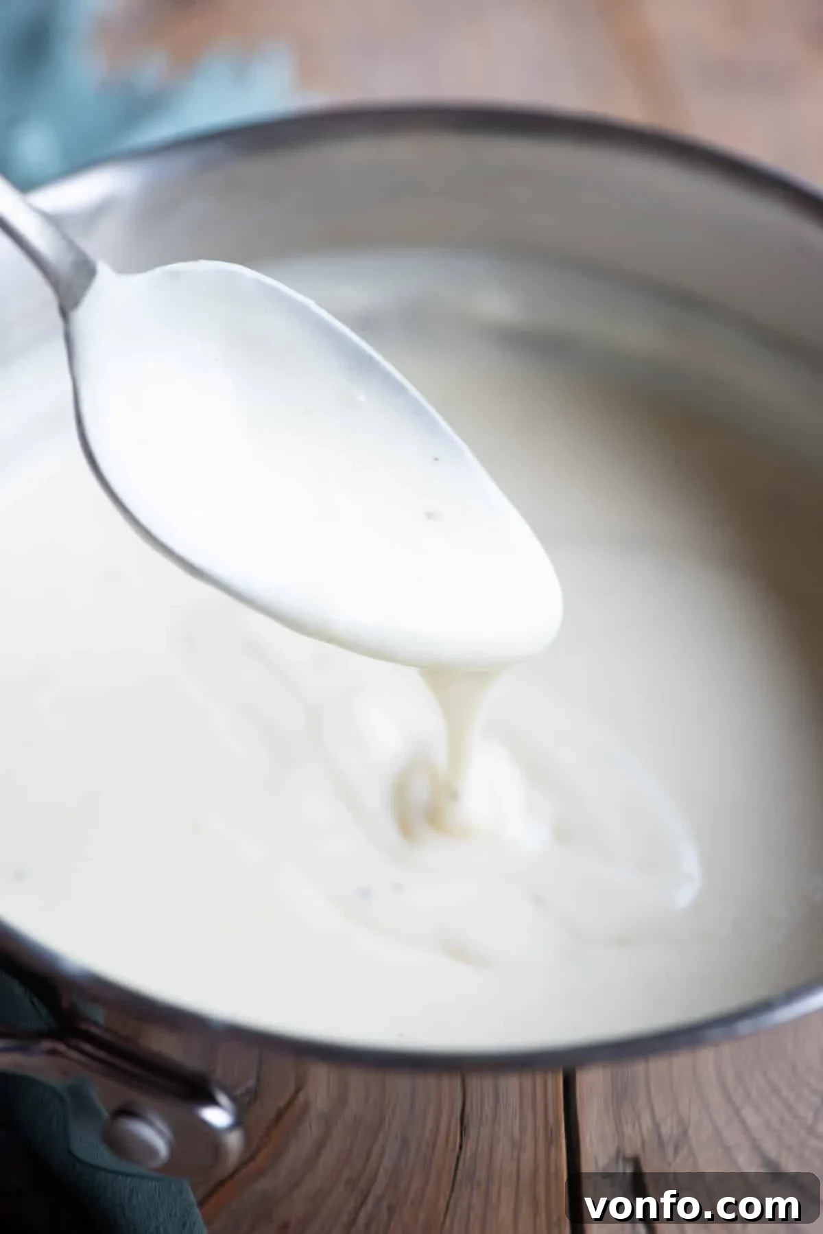Besciamella: The Rich Italian White Sauce 6 A tantalizing close-up of Italian Besciamella sauce, showcasing its luscious, creamy texture as it drips from a spoon back into the pot.